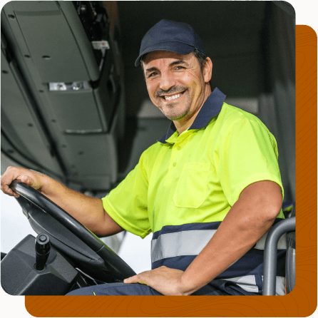 Male worker sitting in large vehicle with one hand on the steering wheel and one hand in his lap.