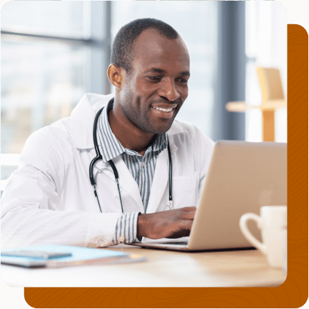 Middle aged male doctor sitting at desk working on laptop.