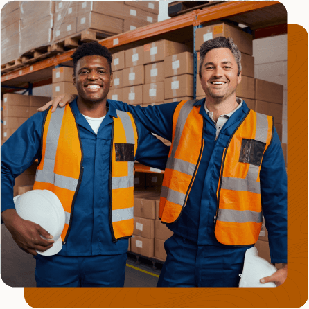 Two male coworkers in uniform with arms around one another in factory.