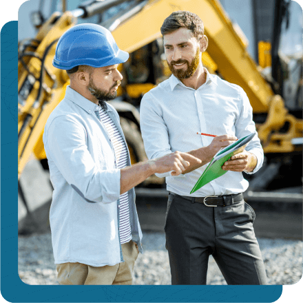 Man in business attire talking with utility worker as they review paperwork in front of them.