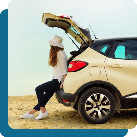 Lady sitting in the trunk of hatchback vehicle looking out into the distance.