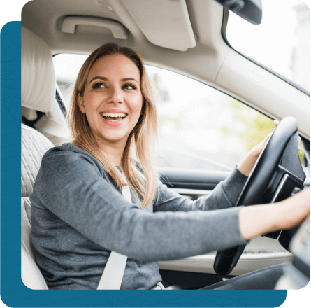 Young female driver sitting in car with one hand on steering wheel and the other on dashboard.