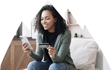 Female sitting in chair in living room using credit card to pay on cell phone.