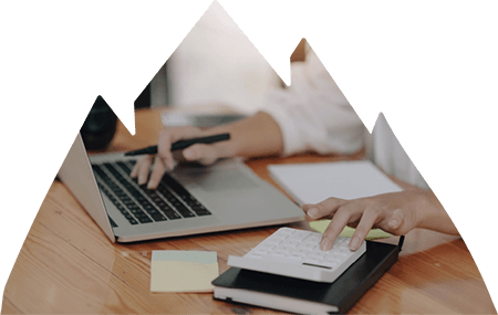 Person working at desk using one hand to navigate laptop and the other a calculator.