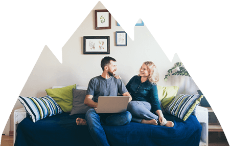 Couple sitting closely on couch in living room looking and smiling at one another.