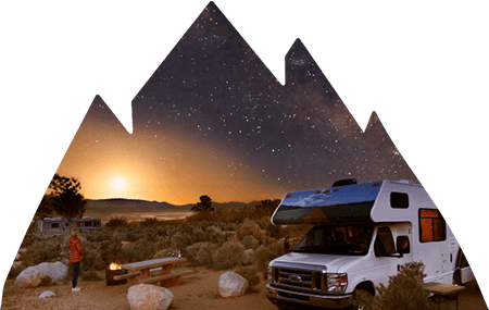 Campsite at dusk with RV in foreground and female standing next to fire.