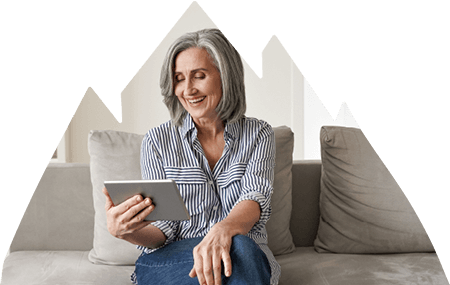 Smiling older woman sitting on couch while using tablet.