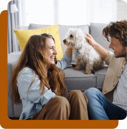 Young couple sitting on floor petting dog on couch.