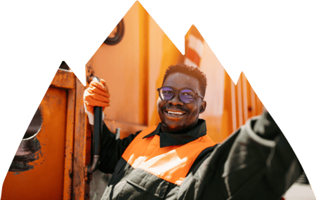 Utility trash worker holding on to side of truck while smiling and waving.