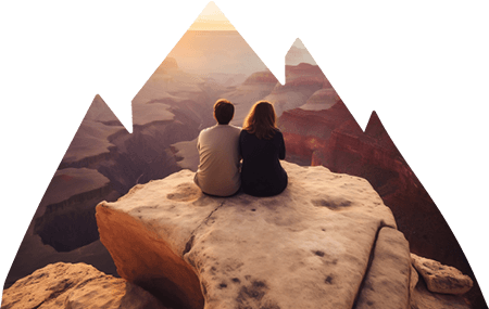 Male and female sitting on edge of rock face looking out into valley and canyons.