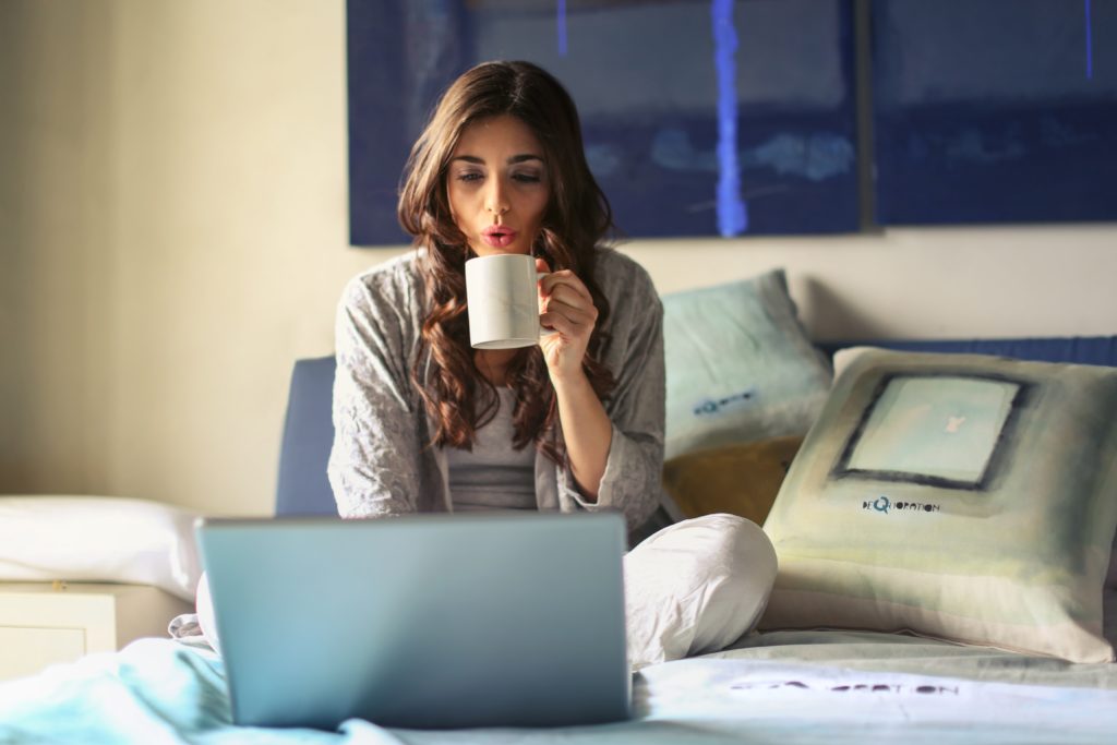 lady drinking coffee and working on her computer in bed
