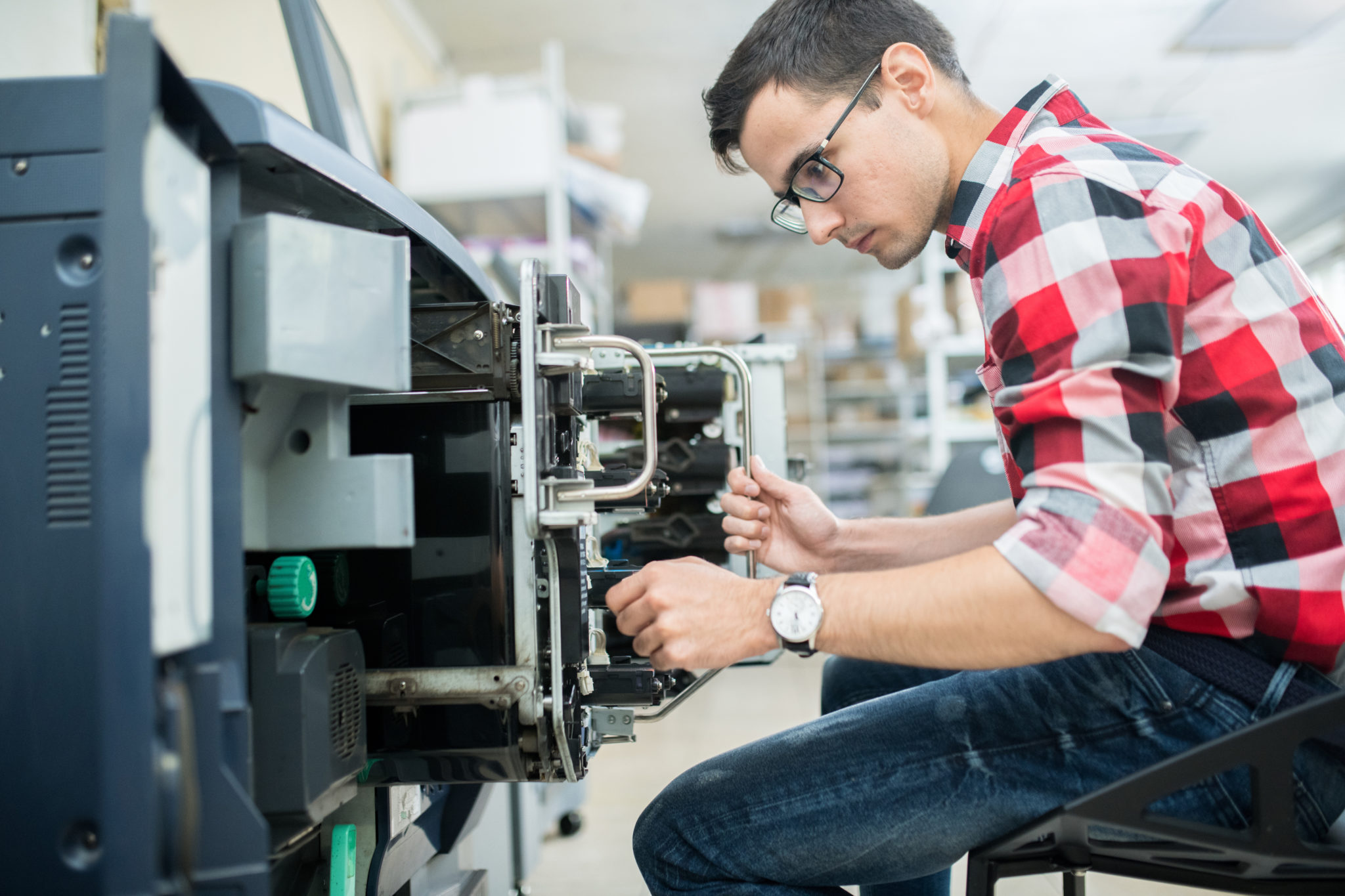 Side view of casual man working with modern printing equipment in typography office