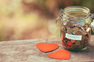 Money jar full of coins for charity and a couple of handcrafted wooden heart shapes. Shallow depth of field. Shot with Canon EOS 5D mark ii.