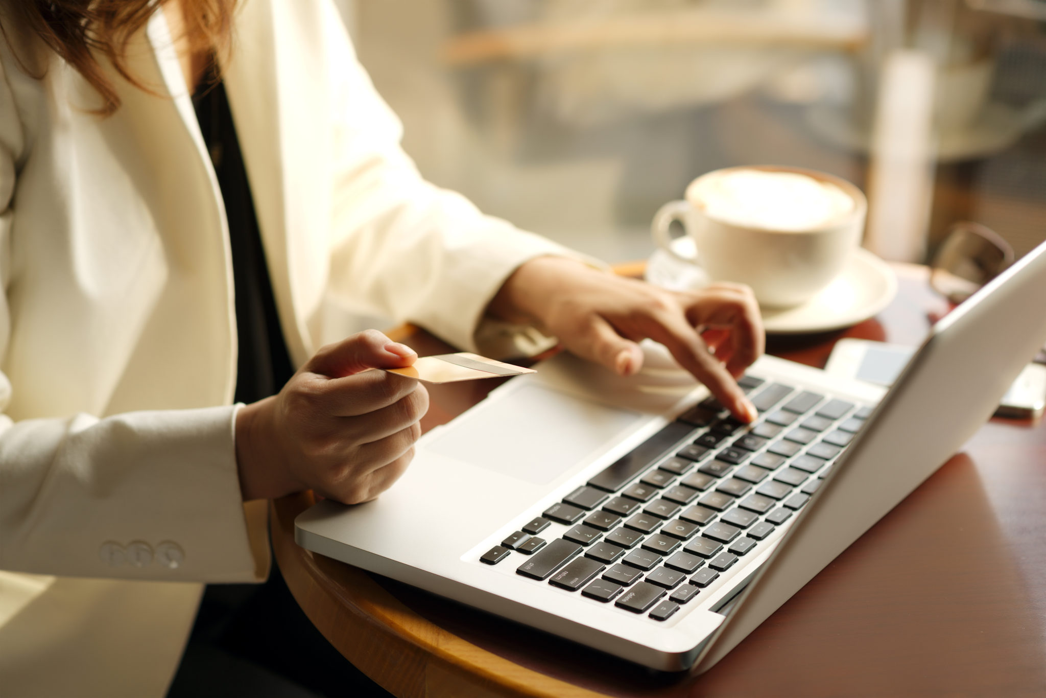 woman in ivory jacket on a laptop holding a credit card